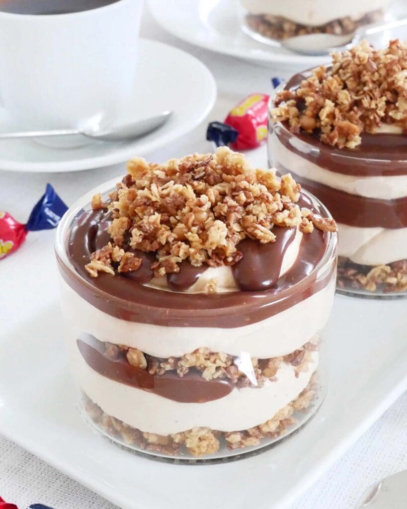 Dumlebiskvier 9 Två glas med lager av dumledessert, grädde och granola på toppen.