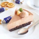 En bit chokladmoussetårta med en slät yta och dekorationer av grädde och citrusfrukter.