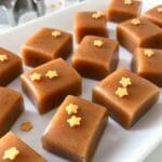 Fyrkantiga bitar av pepparkakskola dekorerade med små stjärnor på en vit tallrik.