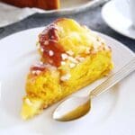 En bit saffransbutterkaka med glasyr och pärlsocker på en vit tallrik med en gaffel.
