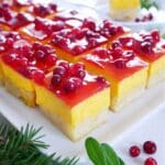 Saffranscheesecake i rutor med ett lager av bär på toppen, serverad på en vit tallrik.