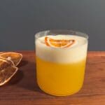 En glas med en gul saffransdrink toppad med en citronskiva och skum.