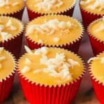 Vit ischoklad med kokosflingor i röda muffinsformar, placerade på en yta.