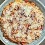 Tallrik med spaghetti täckt av riven ost och tomatsås.