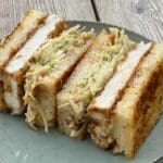 Tre skivor kyckling katsu sando med kål i ett grått fat.