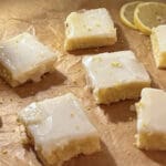 En uppsättning citronblondies med glasyr på ett bakplåtspapper, med citronskivor i bakgrunden.