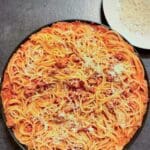 En skål med pasta med salsiccia och riven ost på toppen, serverad på en mörk yta.