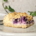 En bit blåbärscheesecake med smulig topping på en tallrik.