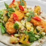 Fisktacos med friterad fisk, ananas, grönsaker och chili på en tallrik.
