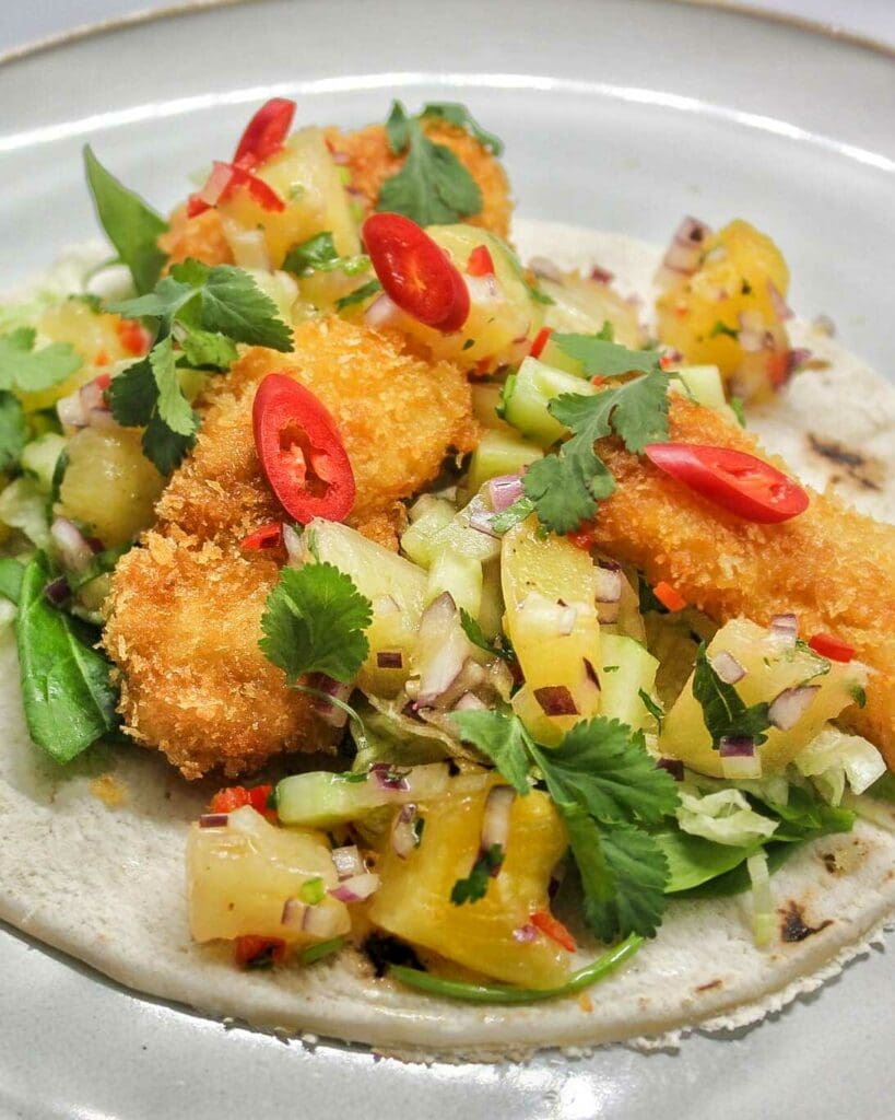 Bacontorsk 7 Fisktacos med friterad fisk, ananas, grönsaker och chili på en tallrik.