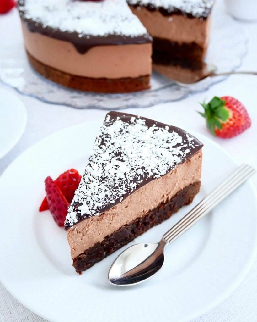 No bake blåbärscheesecake 8 En bit kärleksmums cheesecake med chokladtoppning och kokosflingor på en vit tallrik.