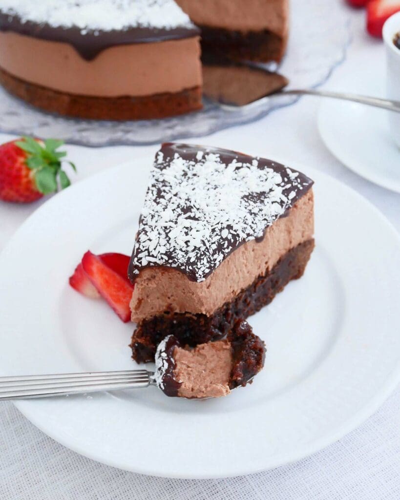 Kärleksmums med extra glasyr 8 En bit kärleksmums cheesecake med chokladtopping och kokosflingor på en vit tallrik.