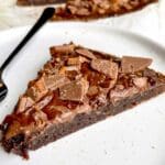 En bit kladdkaka med Daim och chokladglasyr på en tallrik med en gaffel.