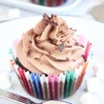 En kladdkakemuffin med chokladfrosting och chokladspån på toppen, i en färgglad muffinsform.