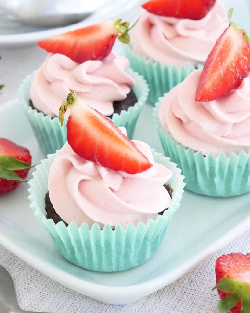 Blåbärsmuffins 9 Fyra kladdkakemuffins med rosa glasyr och skivor av jordgubbar på toppen.