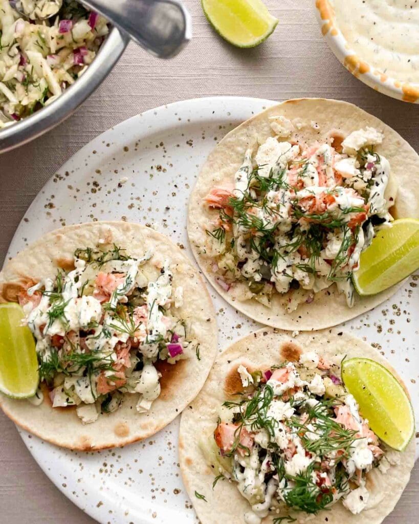 Lättlagad tonfiskbowl 6 Tre lax tacos med grönsaker, sås och limeklyftor på en tallrik.