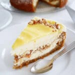 En bit morotscheesecake med citronöverdrag och nötter på toppen, serverad på en tallrik.