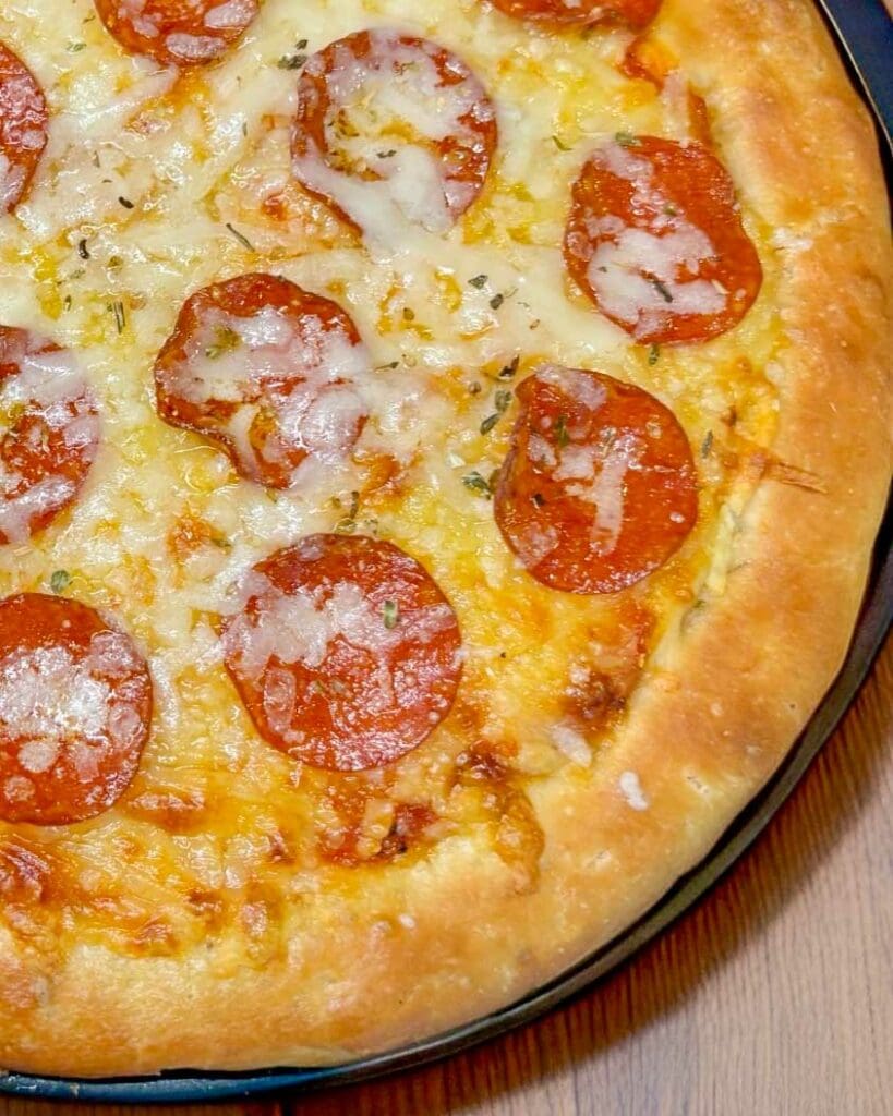 Pizza på västerbottensost och räkor 9 En pizza med pepperoni och smält ost på en rund botten.