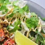 En risnudelsallad med limeklyftor, koriander och krispiga grönsaker på en tallrik.