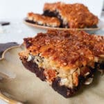 En bit ryttarkaka med chokladbotten och kokosöverdrag på en tallrik.