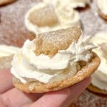 En hand som håller en semmelcookie med grädde och mandelmassa på toppen.