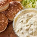 Skål med Big Mac dressing och sesamfröbröd på en träyta med grönsallad.