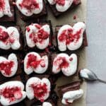 Brownies toppade med vispad grädde och krossade frysta hallon på en bakplåt.