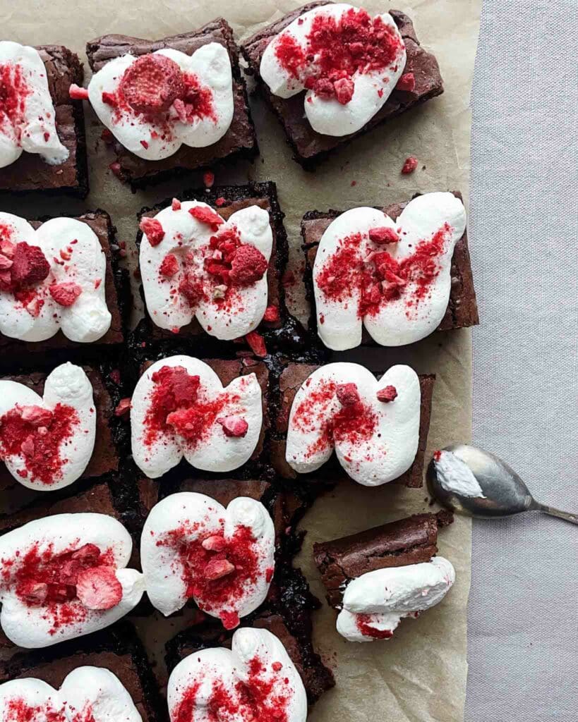 Brownie med brynt smör och mascarponefluff 8 Brownies toppade med vispad grädde och krossade frysta hallon på en bakplåt.