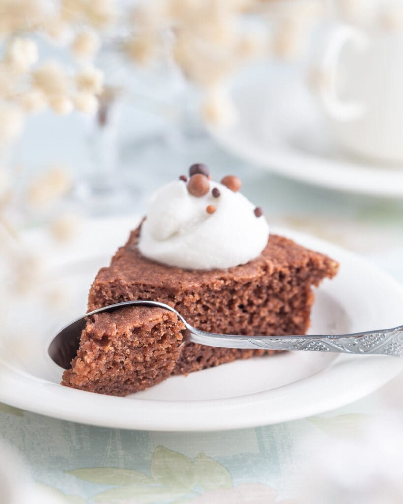 Enkel allergianpassad chokladtårta 13 En bit chokladkaka med grädde och chokladprickar på en tallrik med en sked.