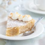 En bit ljus kladdkaka med grädde och kokosflingor på en tallrik med sked.