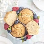 En skål med muffins omgiven av hallon och blåbär, med några muffins delade på mitten.
