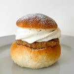 Semla med amaretto och mandelpralin, dekorerad med vispad grädde på en tallrik.