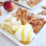 En tallrik med äppelnachos, gräddfil och fruktkompott, med en äpple i bakgrunden.