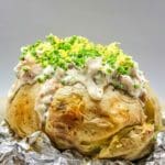 Bakad potatis toppad med skinkröra och grönsaker, serverad på en tallrik.