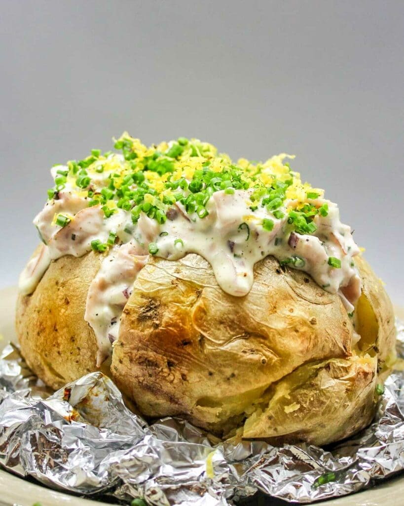 Kycklingröra 9 Bakad potatis toppad med skinkröra och grönsaker, serverad på en tallrik.