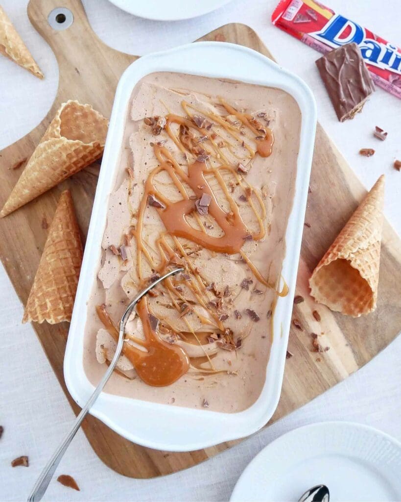 Blåbärsglass 9 En skål med chokladglass toppad med Daim-bitar och kolasås, omgiven av våffelkoner.