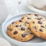 Tre chokladchipkakor med mörka chokladbitar på en ljus tallrik.