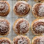 Kanelbullar med en gyllene yta och pärlsocker på toppen, placerade på en plåt.