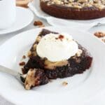 En bit kladdkaka med cookie dough och grädde på en vit tallrik med gaffel.