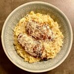 En tallrik med pasta Alfredo toppad med ugnsstekt kyckling och riven parmesan.