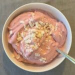 En skål med rosa proteinfluff toppad med hackade nötter.