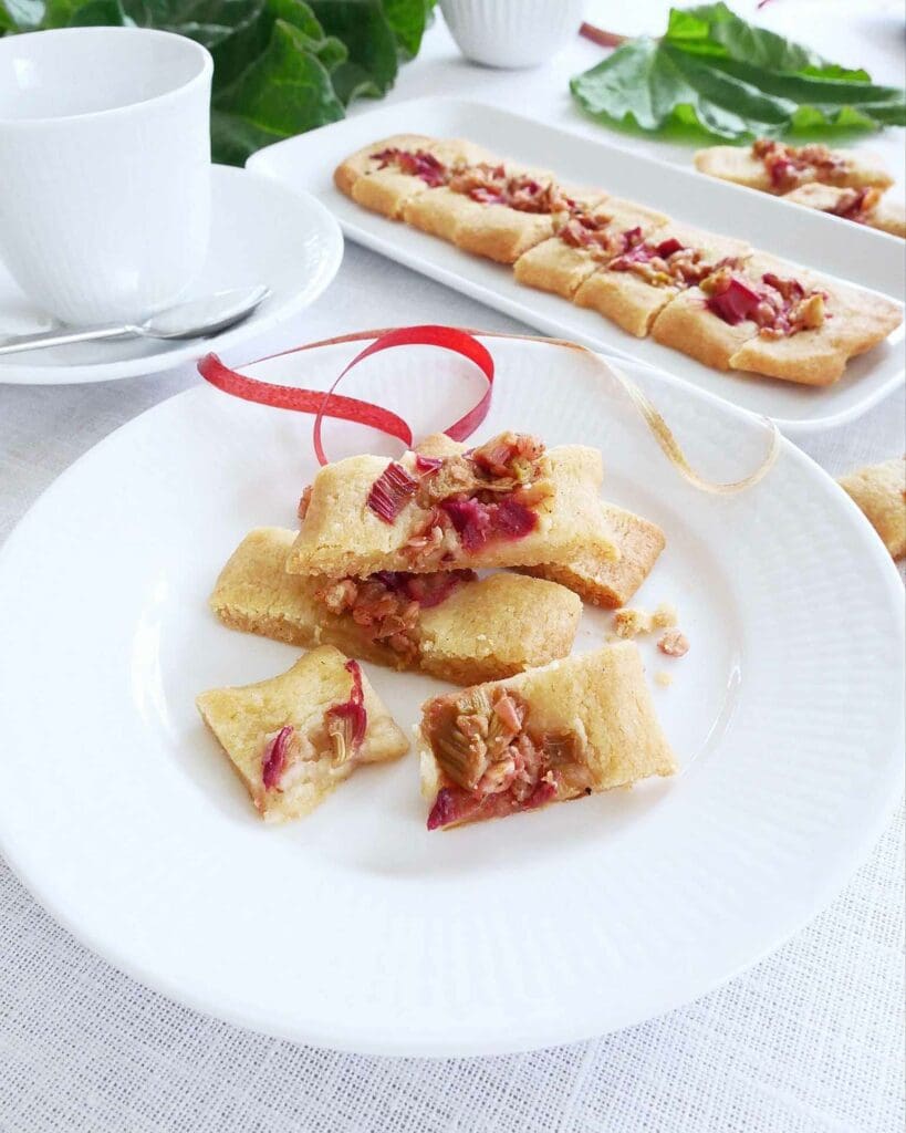 Rabarbermuffins med vaniljkräm & brynt smör 6 Rabarberpajsnittar på en vit tallrik med en kopp i bakgrunden.