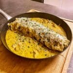 Fläskytterfilé i en stekpanna med krämig kantarellsås och riven ost på toppen.