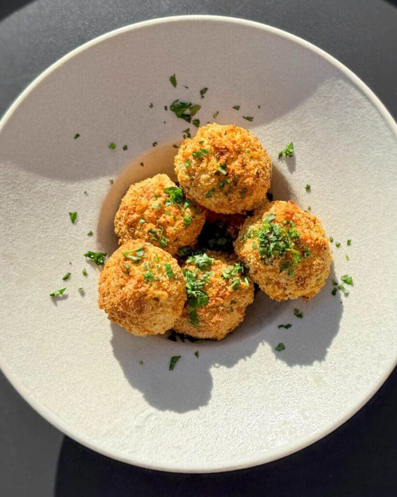 Arancinis 9 En skål med friterade risbollar som är dekorerade med hackad grön persilja.