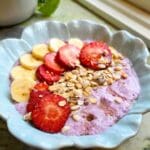 Skål med grekisk yoghurt toppad med skivor av banan, jordgubbar och granola.