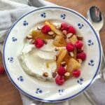 Skål med grekisk yoghurt toppad med smörstekta päron, hallon och mandlar.