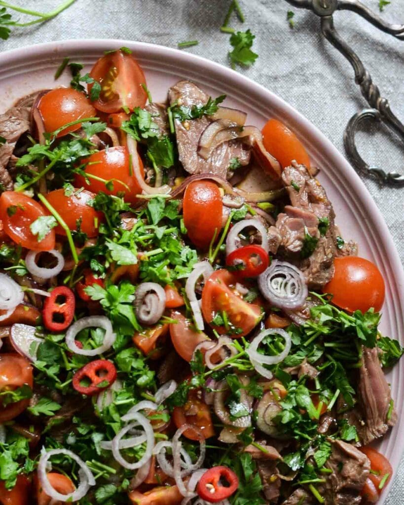 Somrig pastasallad 9 En tallrik med kött, körsbärstomater, lök och färska örter som persilja.