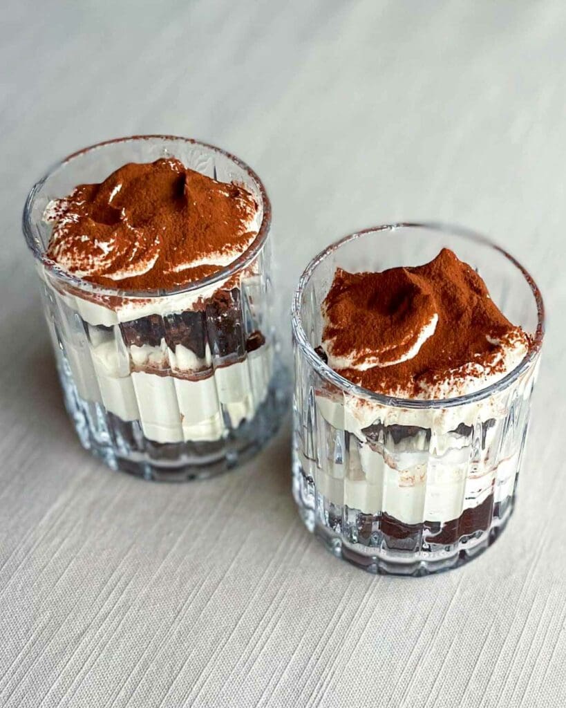 Tiramisubollar 10 Två glas med kladdkakedessert som har tiramisufyllning och ett lager kakao på toppen.