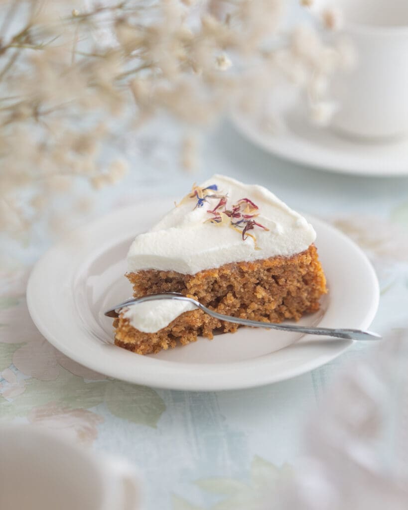 Enkel allergianpassad chokladtårta 11 En bit morotskaka med grädde och ätbara blommor på en tallrik med en sked.