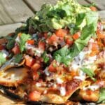 En tallrik med spicy chicken nachos toppad med guacamole, salsa och färsk koriander.